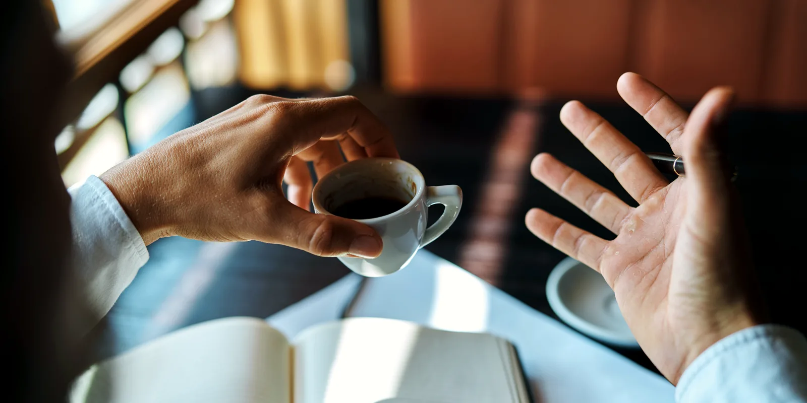 Atemcoach im Gespräch mit einer Klientin am Tisch, zwei Tassen und ein Notizbuch